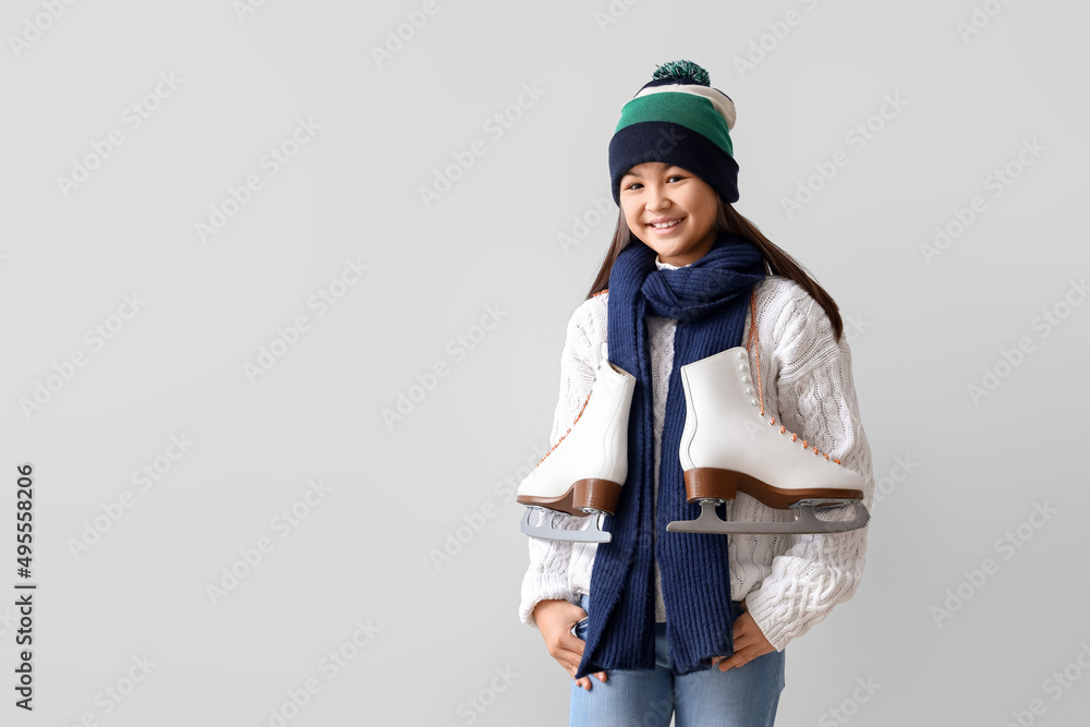 Little Asian girl in warm clothes with ice skates on light background Little Asian girl in warm clothes with ice skates on light background