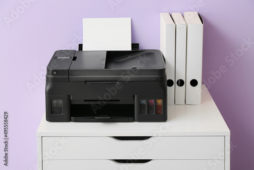 Chest of drawers with printer and folders near color wall