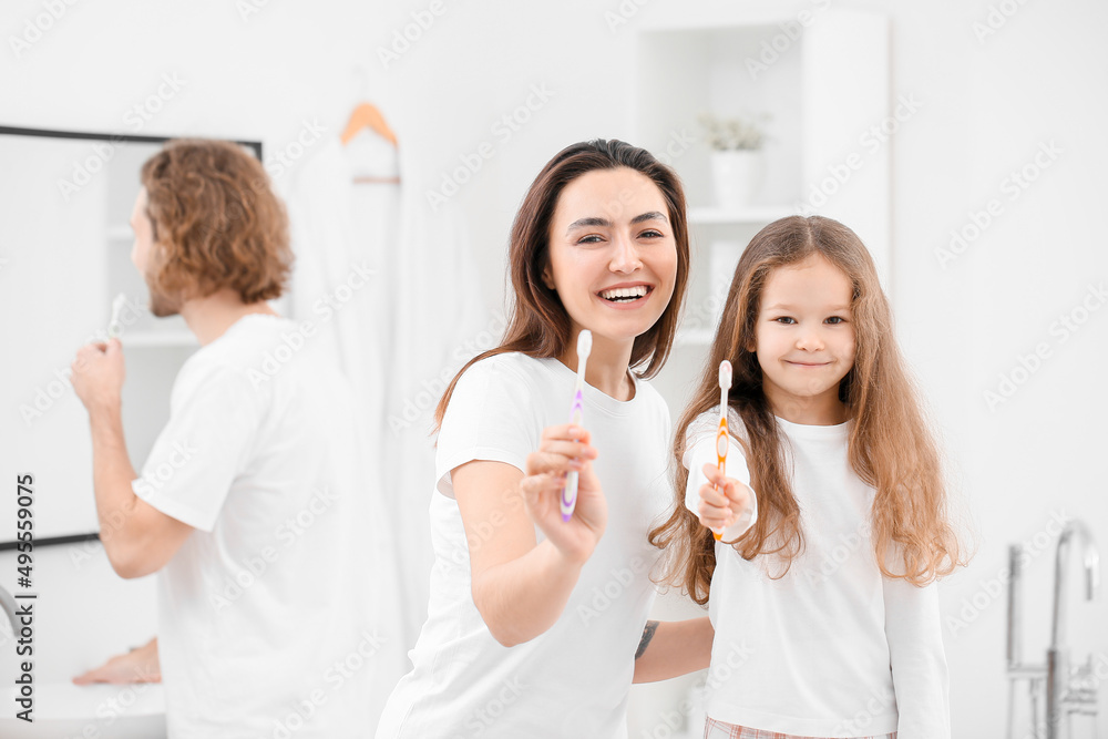 Little girl and her mother with toothbrushes in bathroom