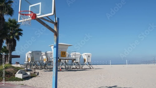 Palm trees and basketball sport field or court on beach, California coast, USA. Streetball playground on shore and lifeguard stand, tower ot station. Mission beach, San Diego. Hoop, backboard and sky.