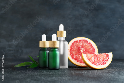 Bottles with essential oil and ripe grapefruit on dark background