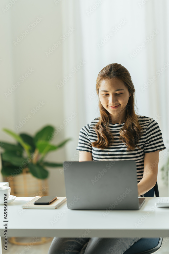 Fototapeta premium Smiling young beautiful Asian woman sitting working laptop computer at home.