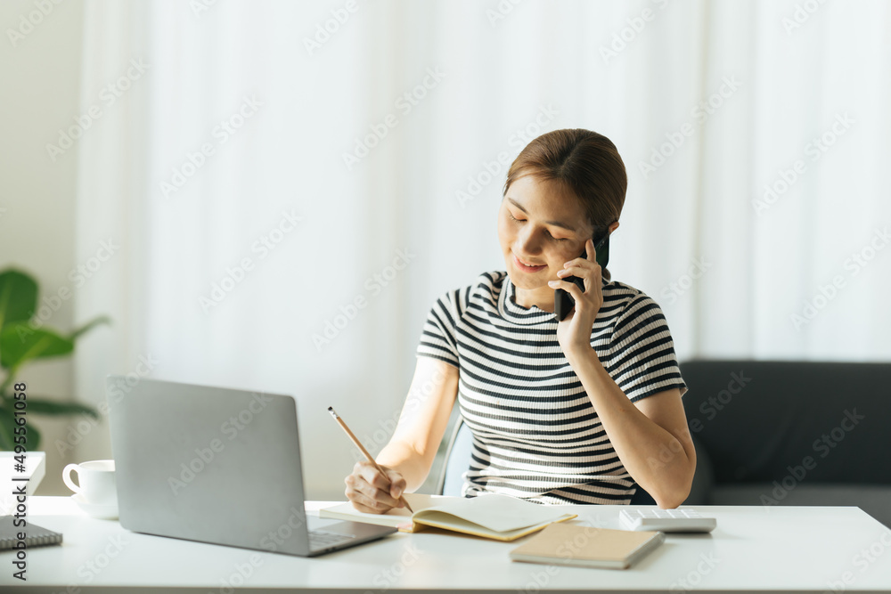 Happy charming woman using smartphone while working with laptop at home