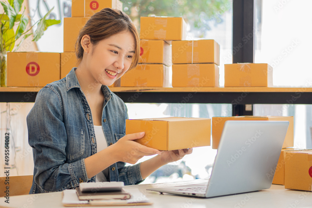 Portrait of a Small Business Startup, SME Owner, Female Entrepreneur Work on boxes and laptops, check online orders to prepare boxes. Selling to customers. Online SME business idea. Portrait of a Small Business Startup, SME Owner, Female Entrepreneur Work on boxes and laptops, check online orders to prepare boxes. Selling to customers. Online SME business idea.