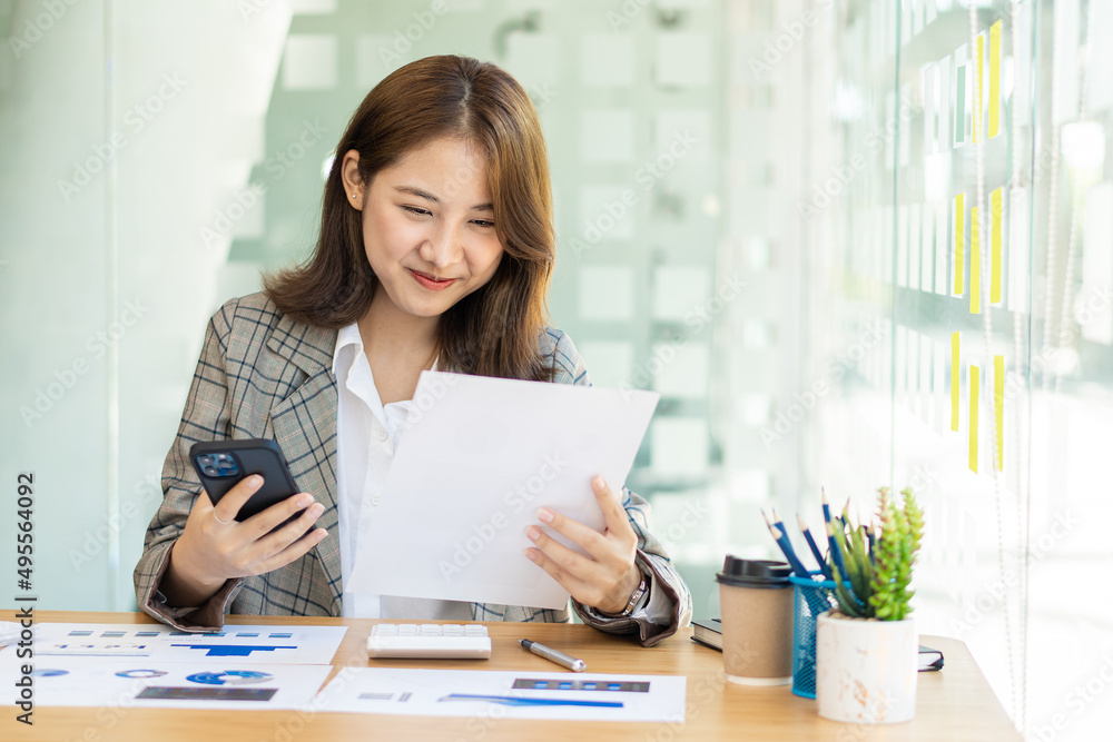 Business Startup Asian woman working with smartphone and graph document with laptop calculator to do analytical calculations. Finance and about real estate investment costs and tax systems. Business Startup Asian woman working with smartphone and graph document with laptop calculator to do analytical calculations. Finance and about real estate investment costs and tax systems.