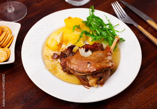 Confit de canard, roasted tasty duck confit with stew potatoes and arugula on a ceramic plate