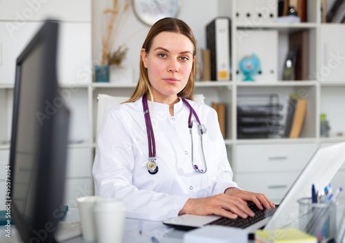 Female doctor in medical uniform is working with documents and laptop