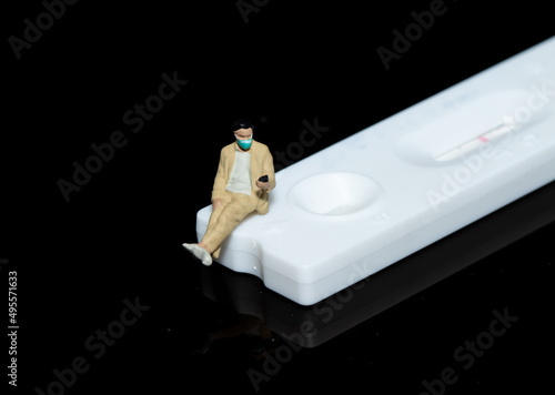 Mini figure doll of a man wearing a medical mask sitting on a cassette rapid test kit.