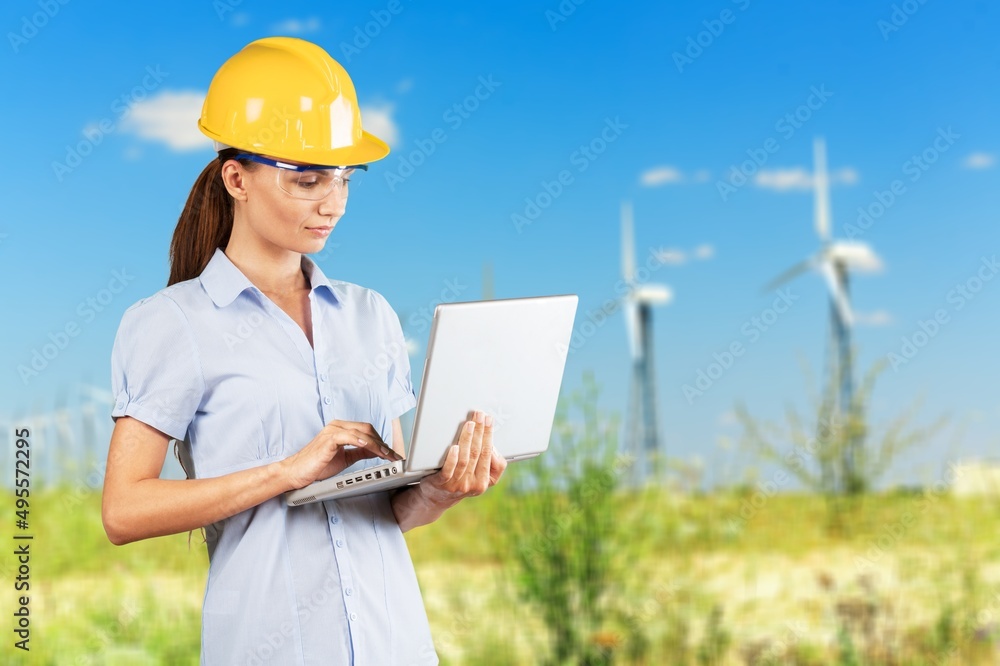 Beautiful man in white helmet working with digital tablet at energy farm. Male inspector controlling functioning of wind turbines outdoors. Beautiful man in white helmet working with digital tablet at energy farm. Male inspector controlling functioning of wind turbines outdoors.
