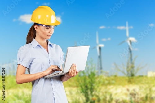 Beautiful man in white helmet working with digital tablet at energy farm. Male inspector controlling functioning of wind turbines outdoors.