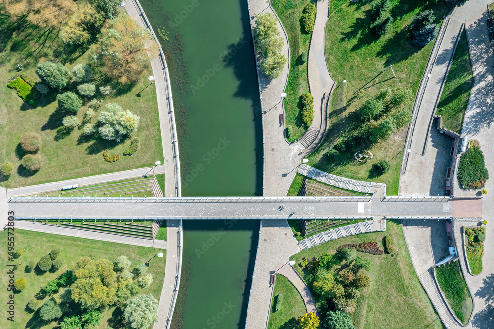 Fototapeta premium walking bridge in the summer park across the river. aerial top view.