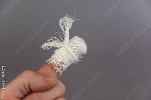 The hand of a mature man with a bandaged index finger. The man holds his palm against the gray background. Health and Medicine.