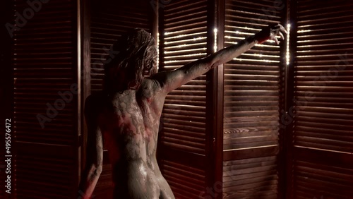 naked female body covered by mud in spa salon, sexy woman is dancing, rear view