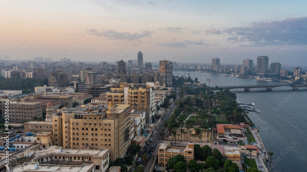 View of Cairo from a height. The Nile skirts an urban area with many buildings.  A bridge over the river is visible. Lilac clouds in the evening pinkish sky. Egypt
