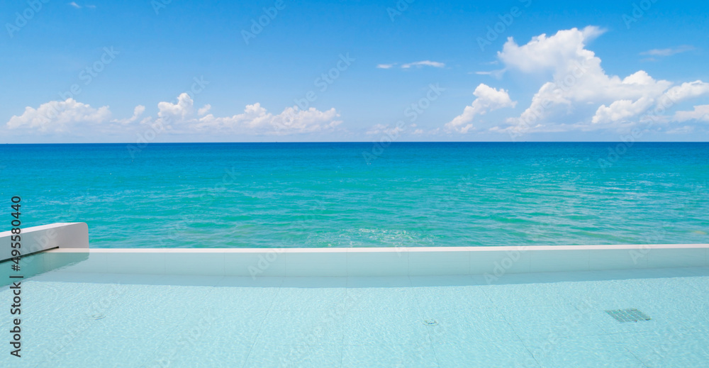Fototapeta premium Swimming pool overlooking view tropical sea and clear blue sky background. Summer holiday and Travel background concept