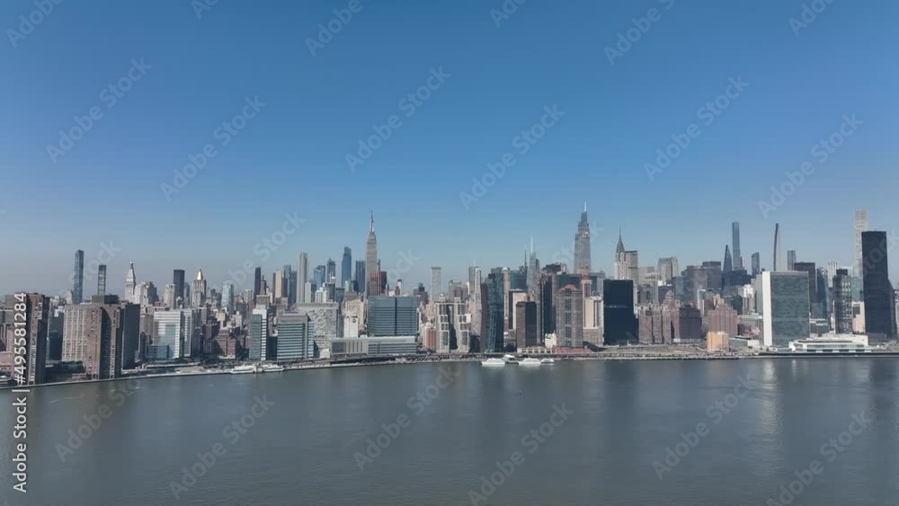 A high angle, aerial view of the Eastside of Manhattan from over Long Island City, NY on a sunny day with clear, blue skies. The drone camera boom up and truck right along the river. A high angle, aerial view of the Eastside of Manhattan from over Long Island City, NY on a sunny day with clear, blue skies. The drone camera boom up and truck right along the river.