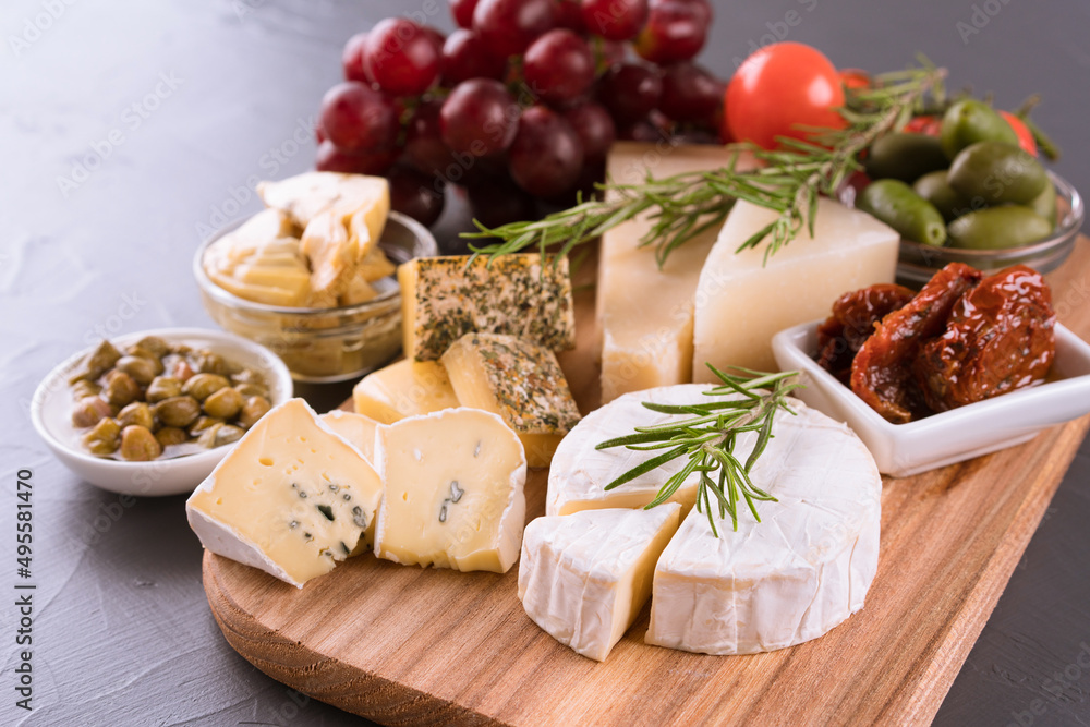 Charcuterie board with cheese. Assortment of antipasti - brie, blue cheese, gorgonzola, camembert, olives, cherry and sun dried tomatoes, artichokes, capers, grape. Cheese platter on gray stone table