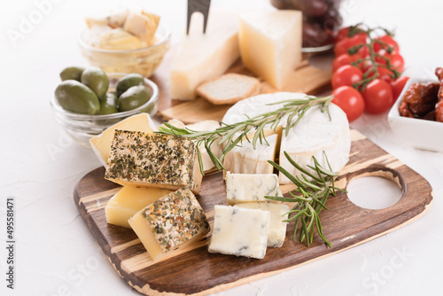 Canvas Print Wooden cheese board with selection of cheeses served together with olives, cherry tomatoes and crackers on white table background