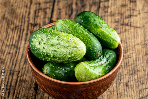 brown bowl of fresh domestic small cucumbers over wooden background. rustic cucumber close up