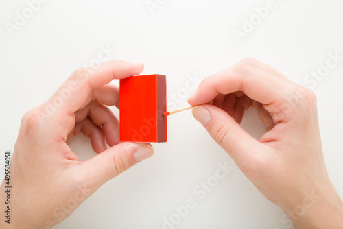 Young adult woman hands holding red box and igniting match stick on white background. Closeup. Point of view shot. Top down view.