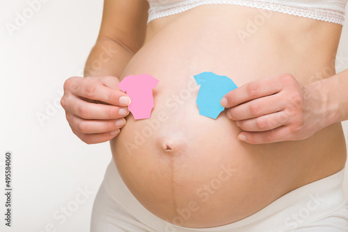 Wallpaper Mural Hands holding shapes of pink and blue bodysuits on young adult pregnant woman big naked belly. Guessing future baby gender. Baby expectation. Closeup. Isolated on light gray background. Torontodigital.ca