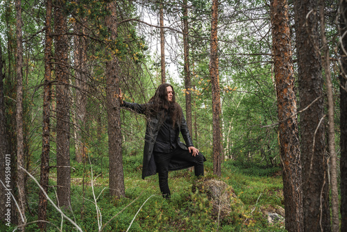 A long-haired man in a black cloak walks in the summer forest. Beautiful summer landscape
