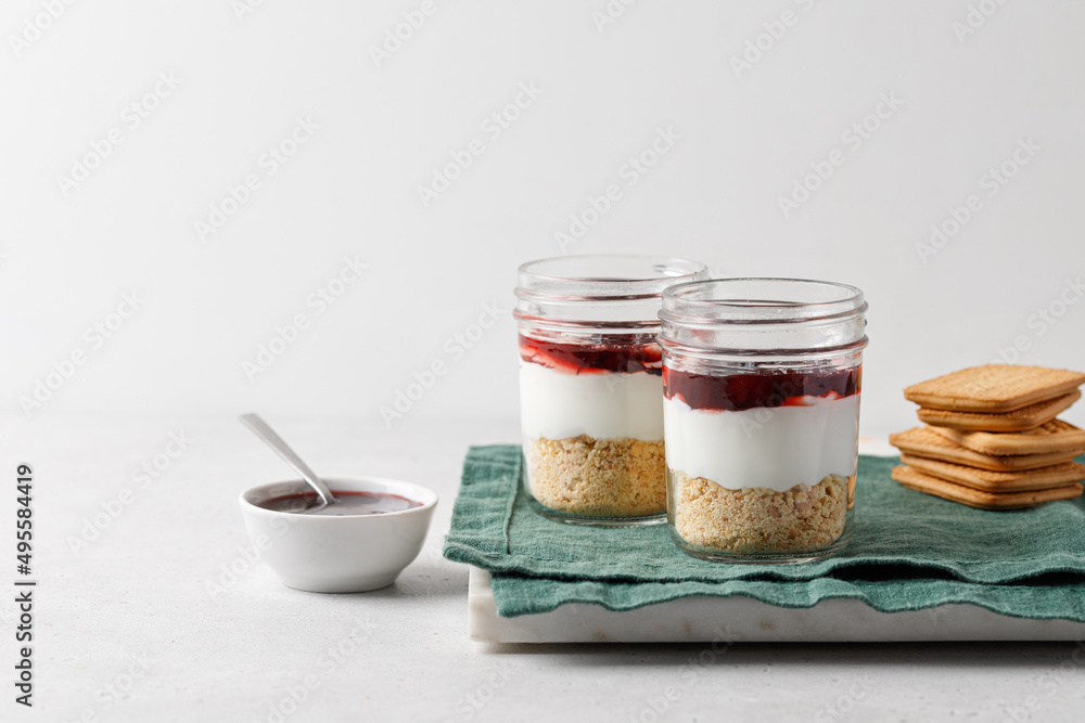 Dessert with yogurt, cookies, jam in a glass jar on green napkin and grey background Dessert with yogurt, cookies, jam in a glass jar on green napkin and grey background