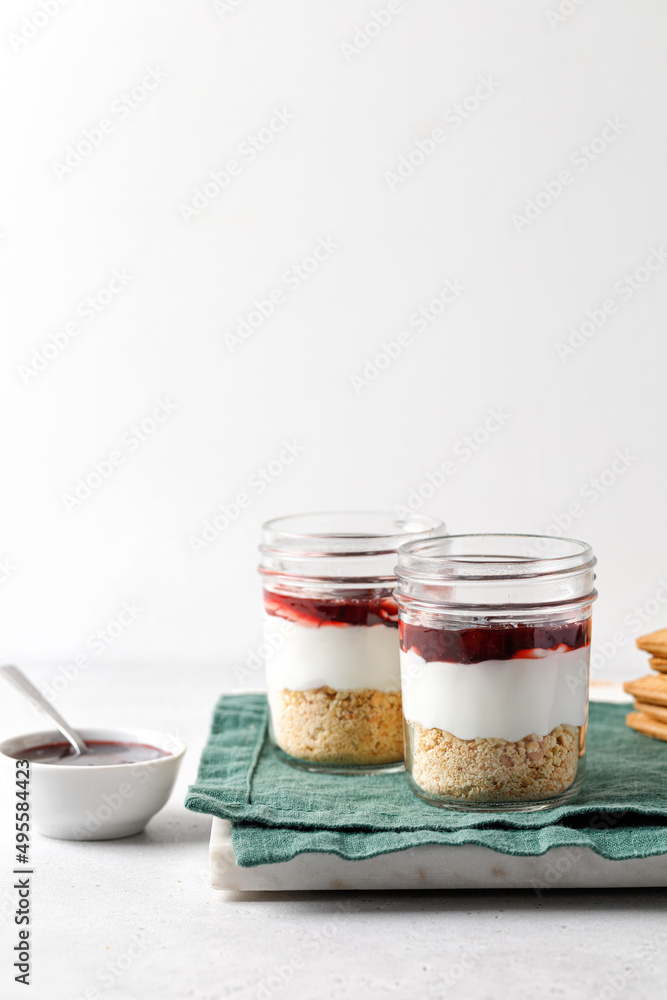 Dessert with yogurt, cookies, jam in a glass jar on green napkin and grey background Dessert with yogurt, cookies, jam in a glass jar on green napkin and grey background