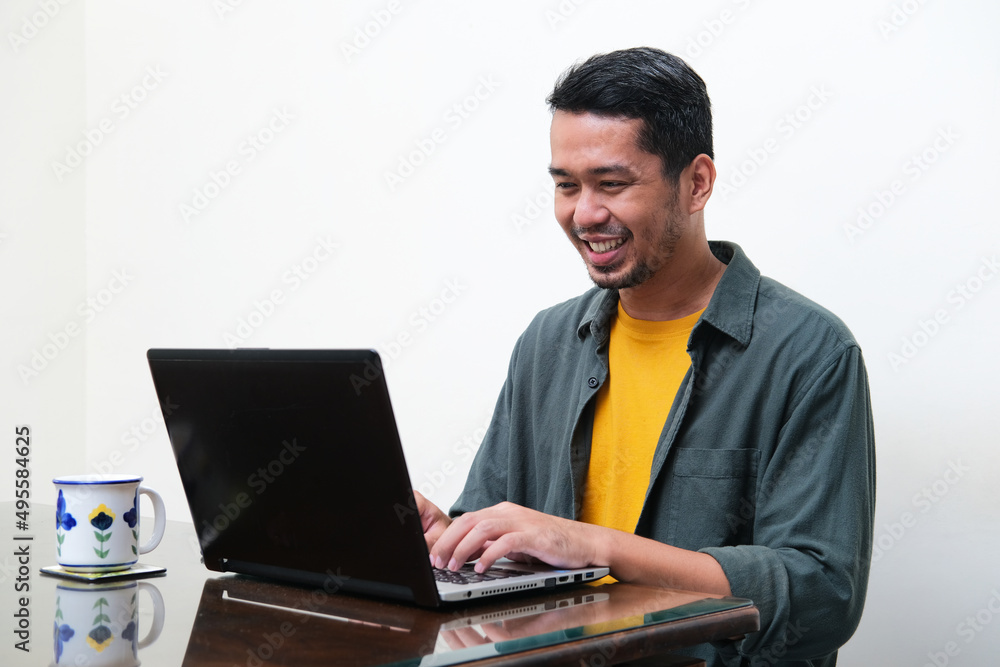 Adult Asian man smiling happy when typing on his laptop Adult Asian man smiling happy when typing on his laptop