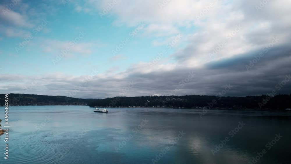 Wide angle panoramic aerial shot of a commuter ferry crossing dark calm waters, blue skies Wide angle panoramic aerial shot of a commuter ferry crossing dark calm waters, blue skies