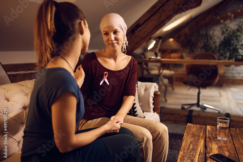Smiling woman with breast cancer talks to her female friend at home.