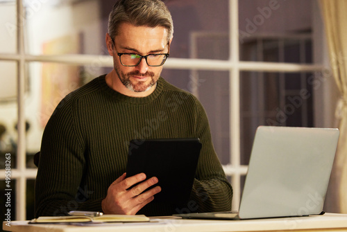 Determined to make his business a success. Cropped shot of a handsome mature businessman working on his laptop and tablet at home.