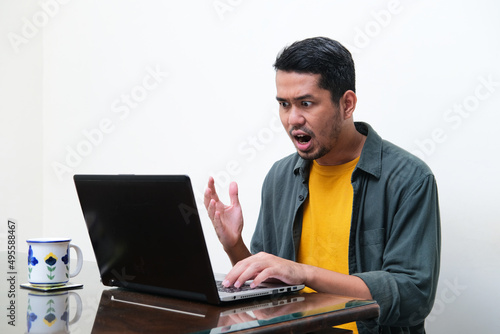 Adult Asian man showing angry expression in front of his laptop photo