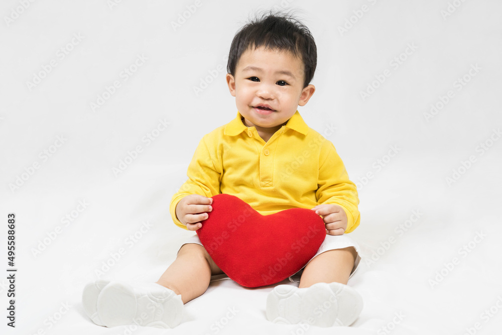 Asian cute baby boy about one year old in yellow shirt sitting and smile with red heart shape pillow isolated on white Selective focus. Asian cute baby boy about one year old in yellow shirt sitting and smile with red heart shape pillow isolated on white Selective focus.