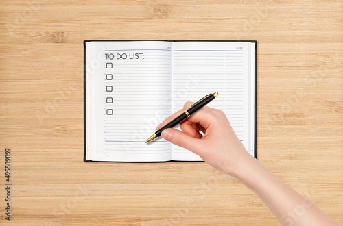 A woman's hand makes a list of things to do and tasks in a notebook. Top view of the desktop. The concept of time planning and self-organization photo