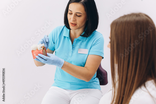Girl sitting on a dental chair on a visit to the female dentist, showing a caries on the model.