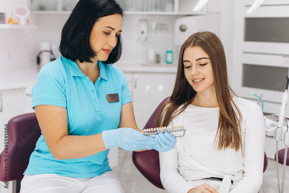 Fototapeta premium A female dentist helps her patient choose the color of the implant or crown using a color scale