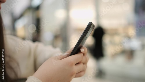 Young woman standing in a shopping mall with a smartphone. Lui in the background. Busy shopping center. Finding information on your smartphone photo