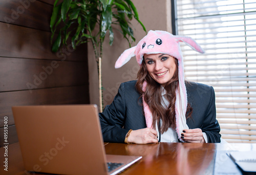 Business lady with cheerful easter bunny hat celebrates easter at work. Woman leader or student is having fun.