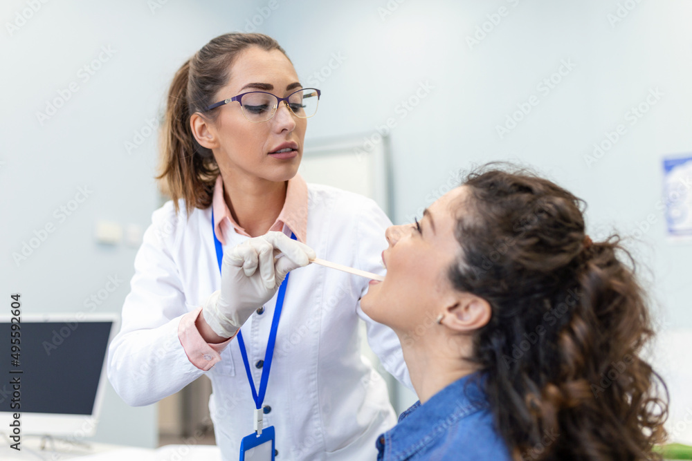 Female patient opening her mouth for the doctor to look in her throat. Female doctor examining sore throat of patient in clinic. Otolaryngologist examines sore throat of patient.
