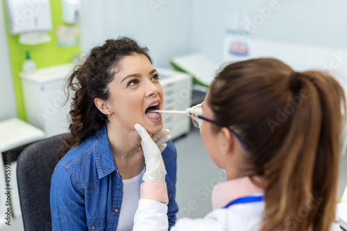 Doctor with depressor checking sore throat. Experienced doctor examines adult woman for sore throat