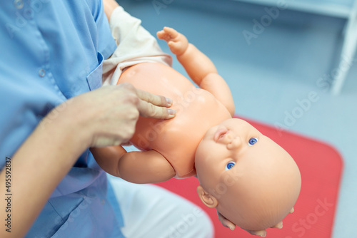 Woman performing CPR on baby training doll with one hand compression. First Aid Training - Cardiopulmonary resuscitation. First aid course on cpr dummy. photo