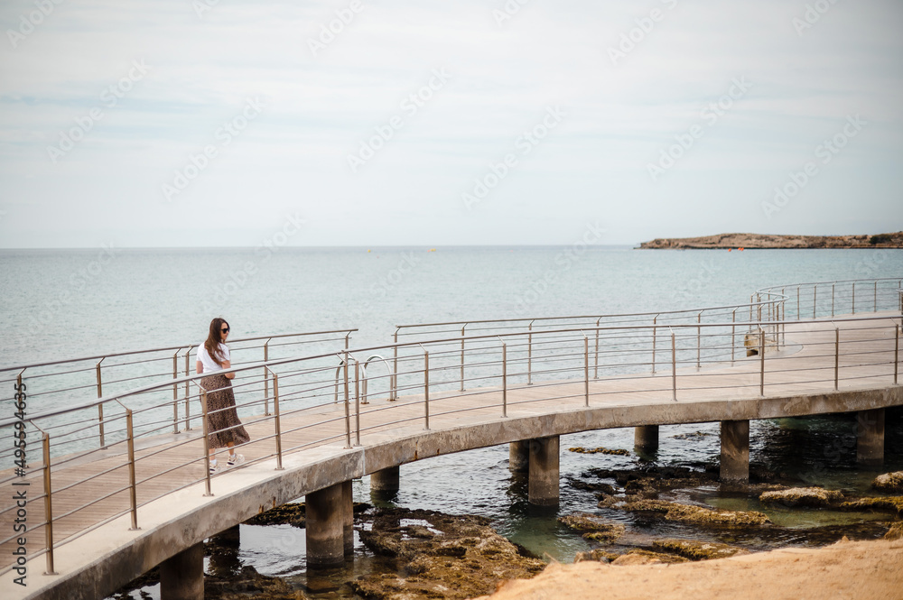 Attractive woman in sunglasses walking on pier near seashore