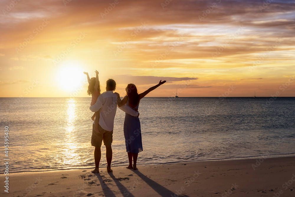 Fototapeta premium A happy family with outstretched arms on vacation stands on a beach during sunset time