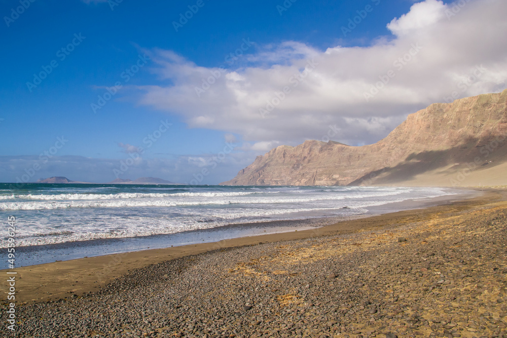 A view of the beach (Playa) in Famara, Lanzarote. At the back of the beach are the high cliffs (Risco) and on the horizon the island of La Graciosa.