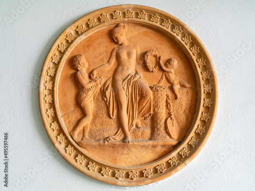 Terracotta tondo with young naked woman and two children with flower wreaths, round bas-relief emblem photo