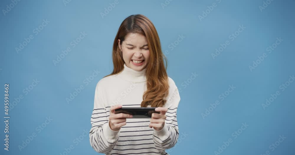 Youth attractive cheerful Asia lady excited enjoy looking at smartphone play mobile game stand isolated over blue background. Play game on smartphone winning victory moment, Empty copy space concept. Youth attractive cheerful Asia lady excited enjoy looking at smartphone play mobile game stand isolated over blue background. Play game on smartphone winning victory moment, Empty copy space concept.