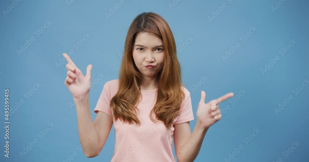 Youth attractive Asia lady with smile wear pink casual questioned consider crosses arms and points sideways chooses between two options isolated on blue background. Girl indicates left and right. Youth attractive Asia lady with smile wear pink casual questioned consider crosses arms and points sideways chooses between two options isolated on blue background. Girl indicates left and right.