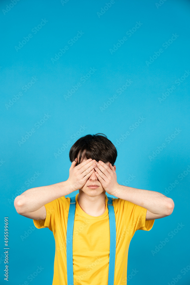 Adolescent covering his eyes with hands isolated on blue background. Puberty problems concept. Adolescent covering his eyes with hands isolated on blue background. Puberty problems concept.