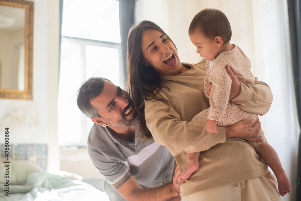 Excited mid adult couple having fun with baby son at home. Parents holding little child and laughing in bedroom in morning. Family at home concept Excited mid adult couple having fun with baby son at home. Parents holding little child and laughing in bedroom in morning. Family at home concept
